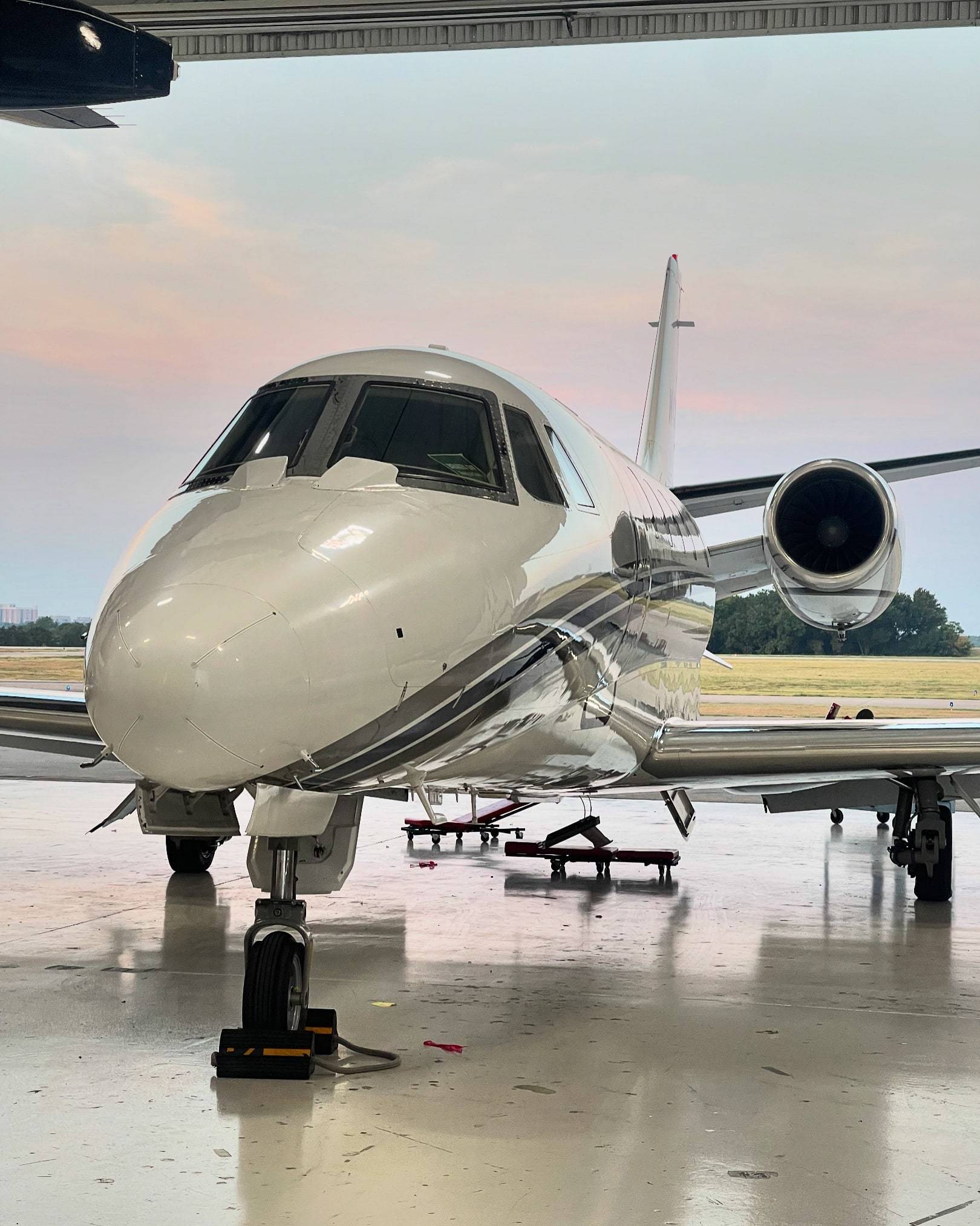 Cessna Citation parked at the open hangar door at dusk, pink sky and airfield behind