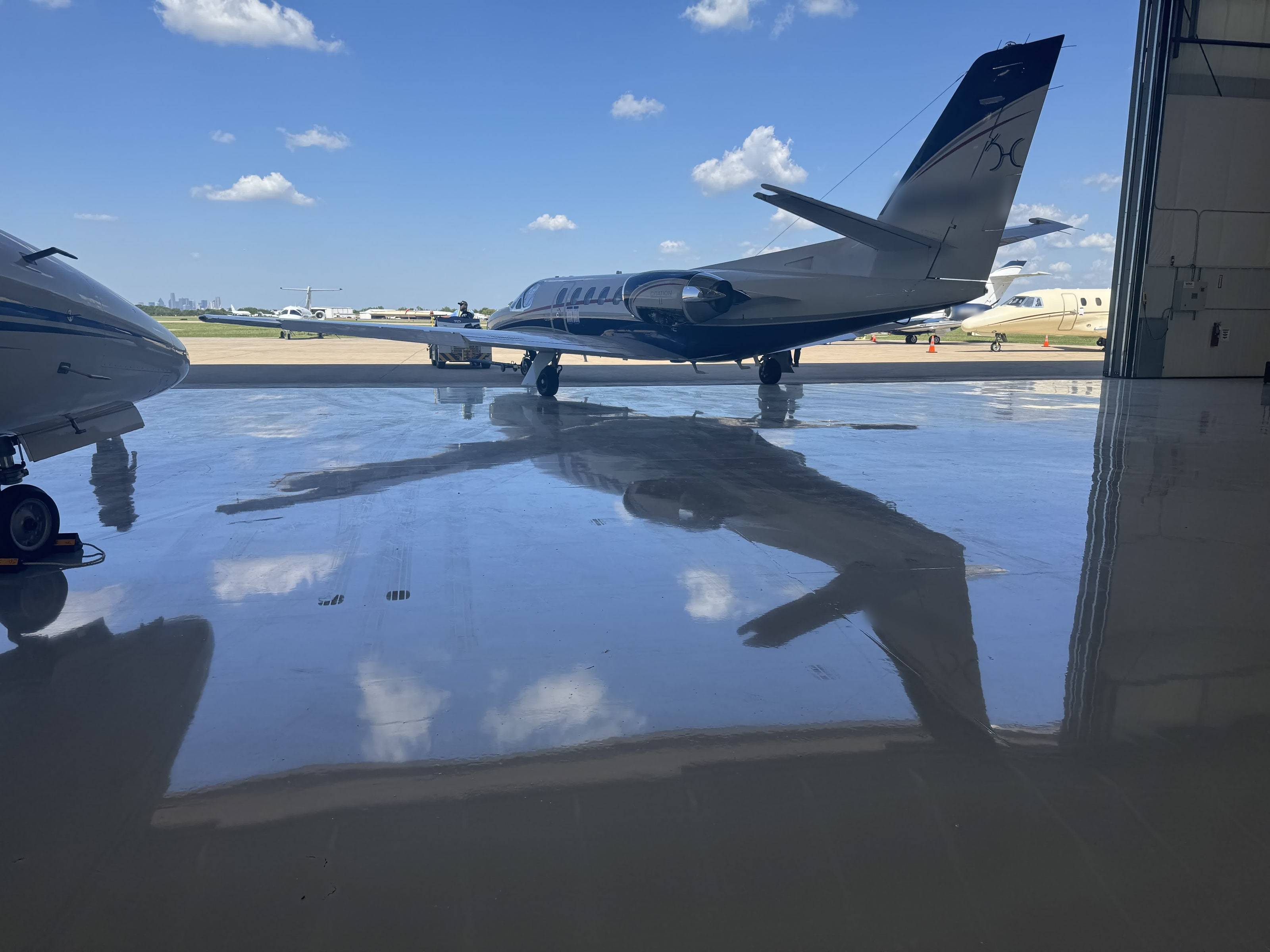 Citation II on the ramp seen from inside the hangar, mirrored in the polished floor, Dallas skyline beyond