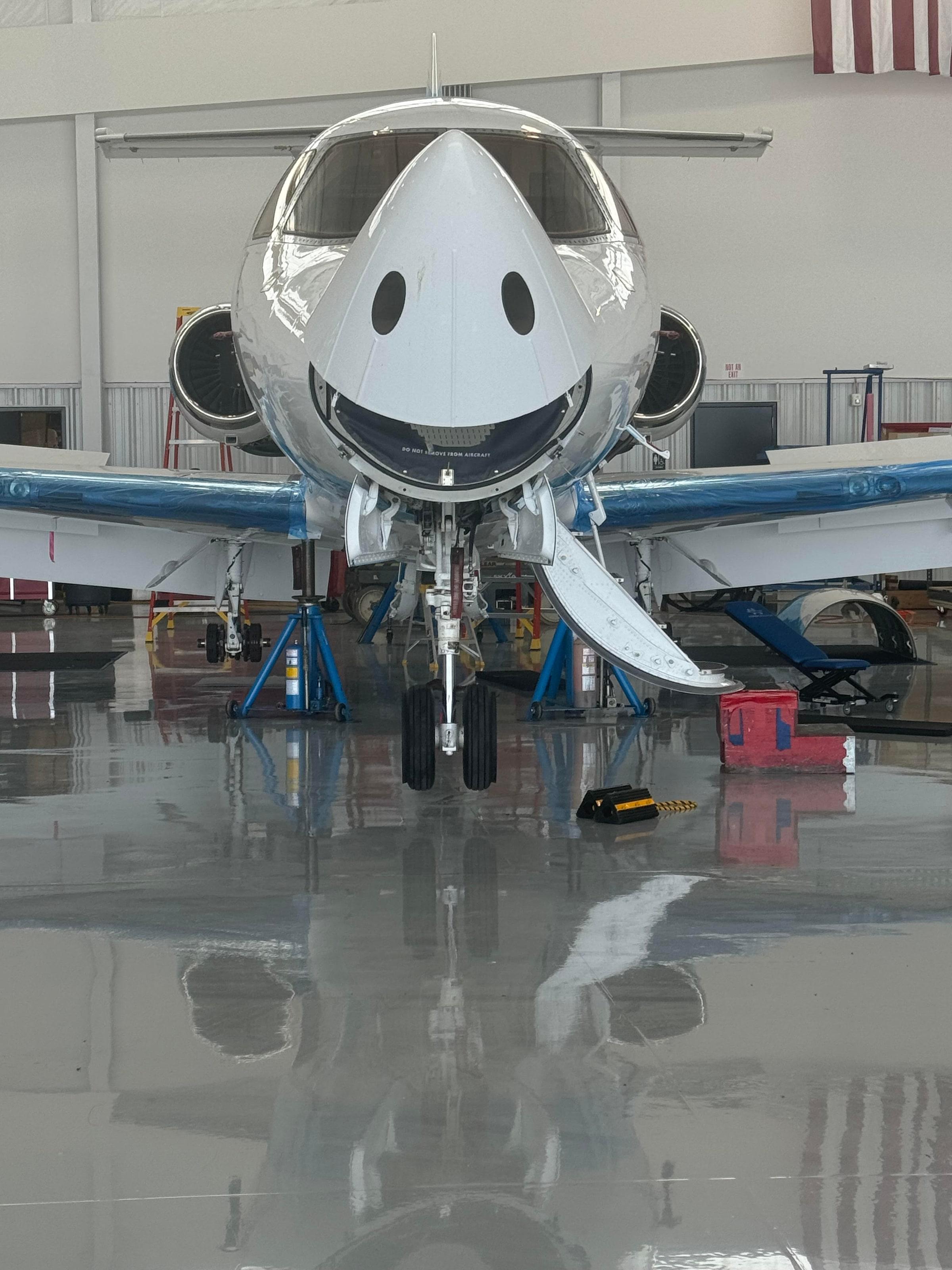 Hawker 400 on jacks in the hangar, head-on, with a smiling face on its nose and the airstair down