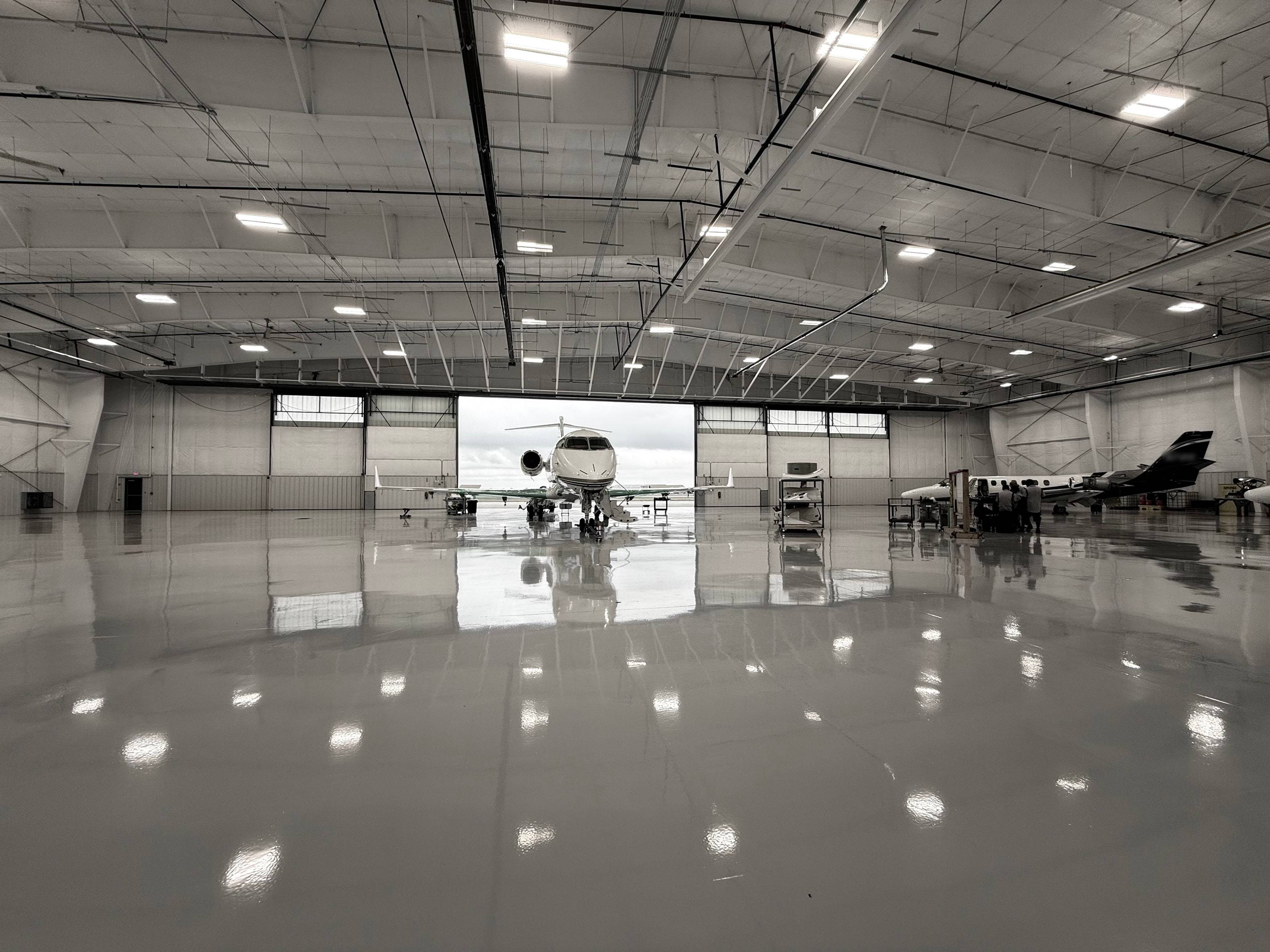 Wide hangar interior, a business jet framed in the open doorway and mirrored in the polished epoxy floor