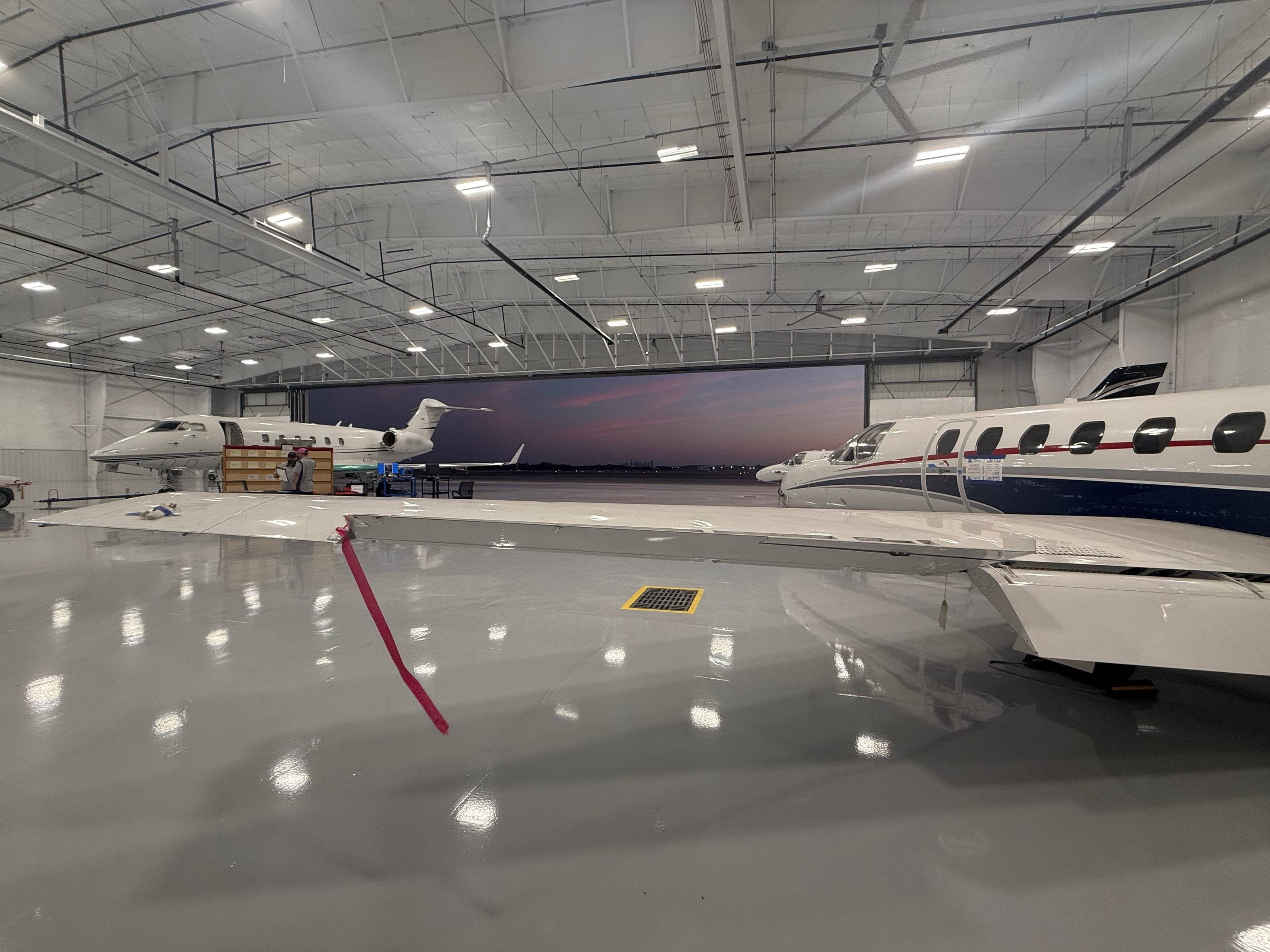 Inside the Jets MRO hangar at dusk, doors open to a pink sky, a jet wing and the polished floor in the foreground