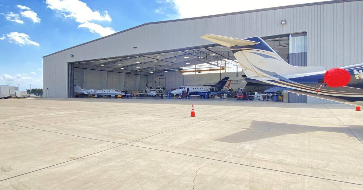 Jets MRO hangar with doors open and business jets inside, a jet tail and traffic cones on the ramp in front