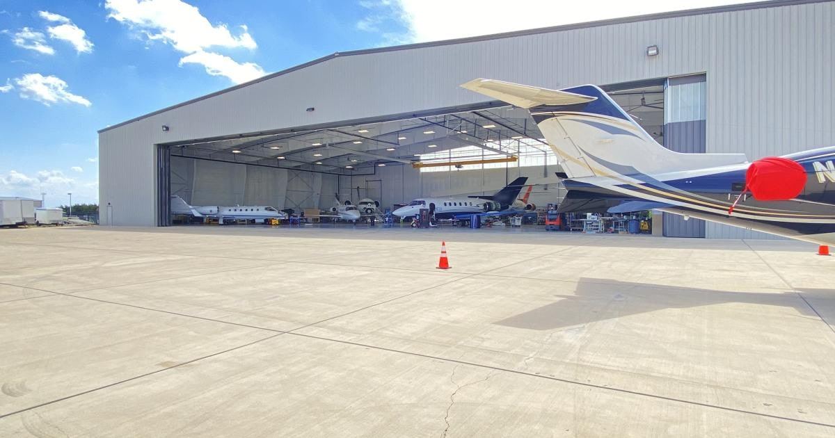 Jets MRO hangar with doors open and business jets inside, a jet tail and traffic cones on the ramp in front