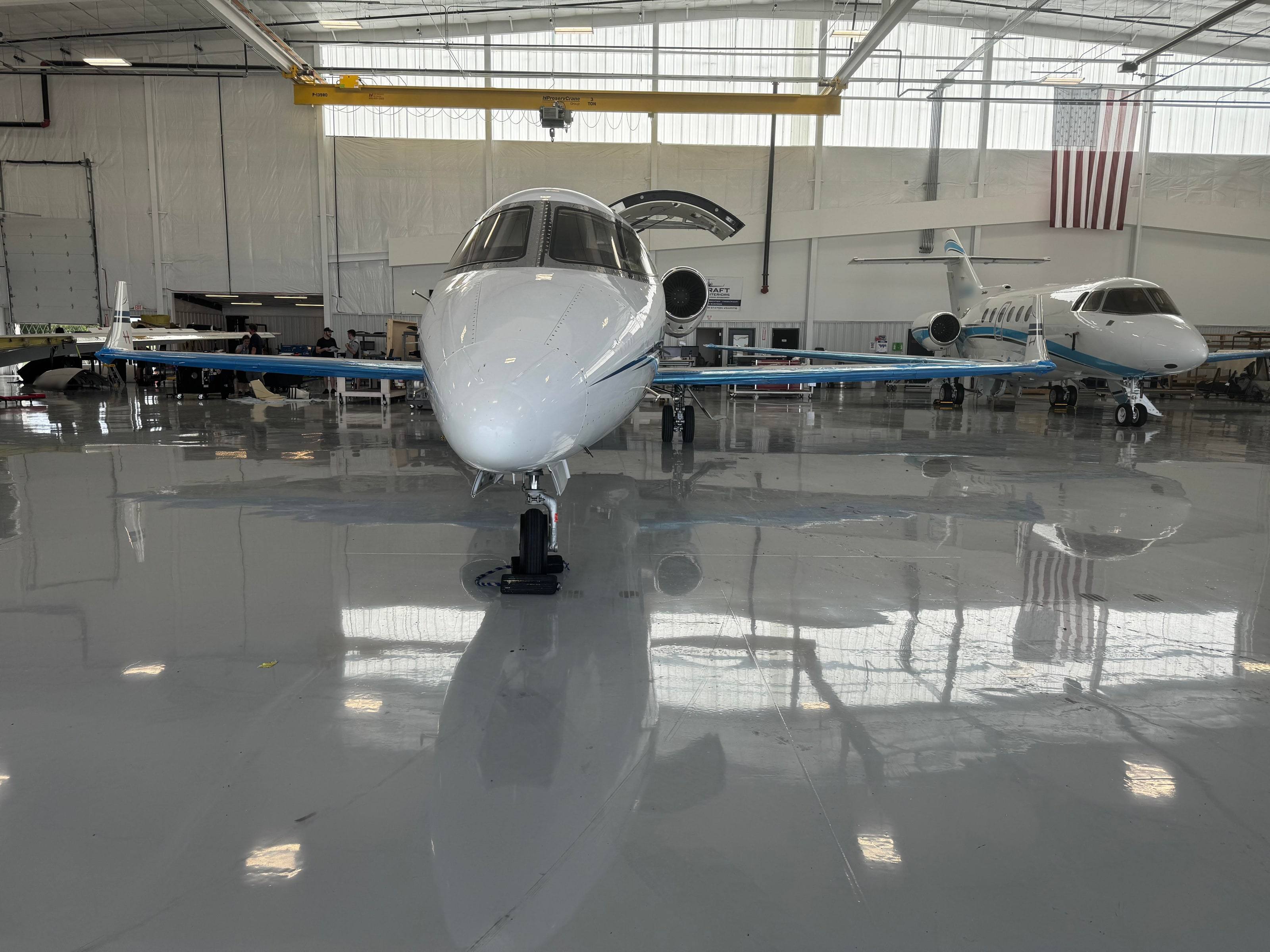Learjet head-on on the reflective hangar floor, upper door open, wings wrapped in protective film