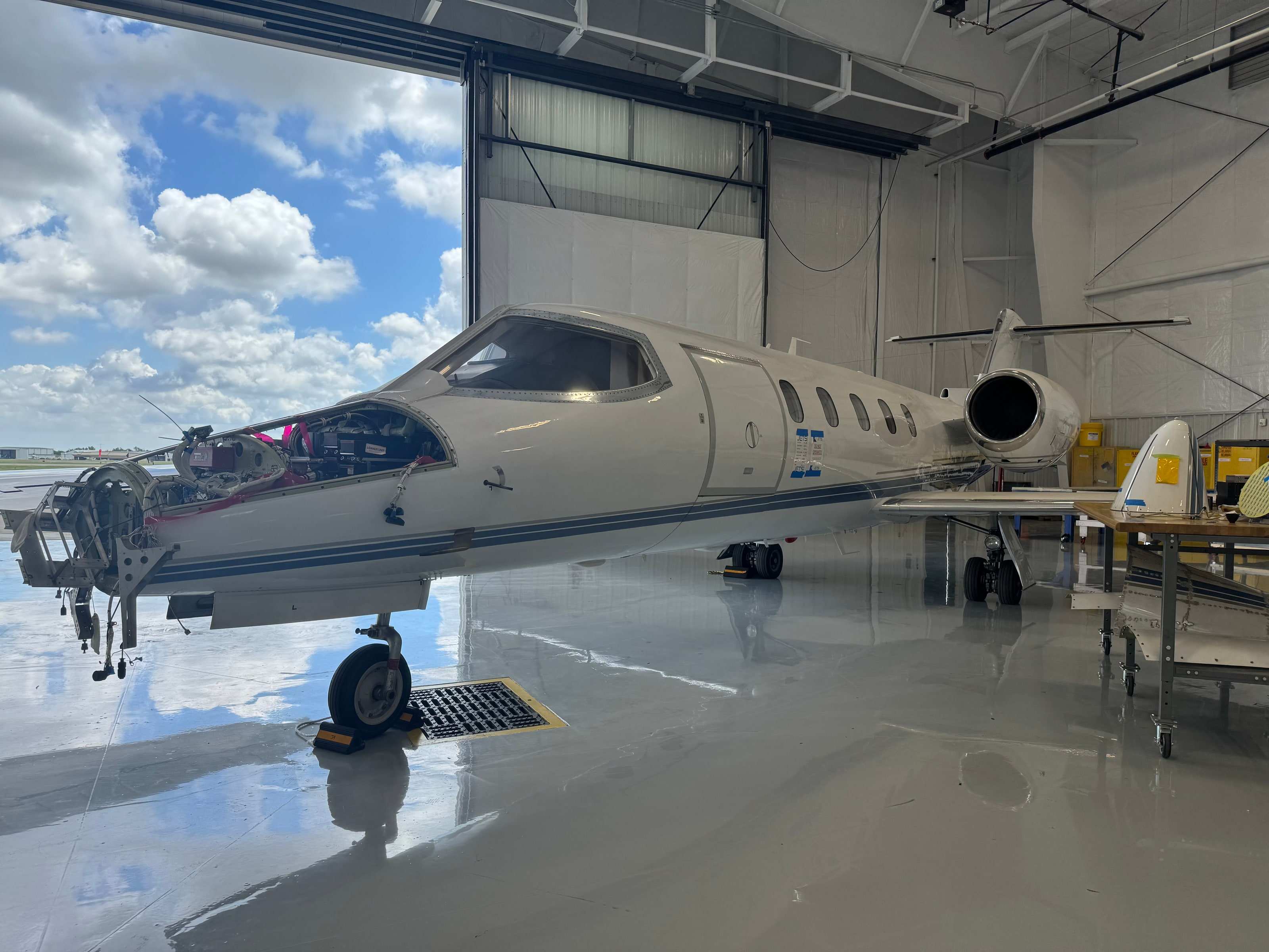 Learjet in the hangar with its radome removed, exposing the nose avionics bay; hangar door open to the sky