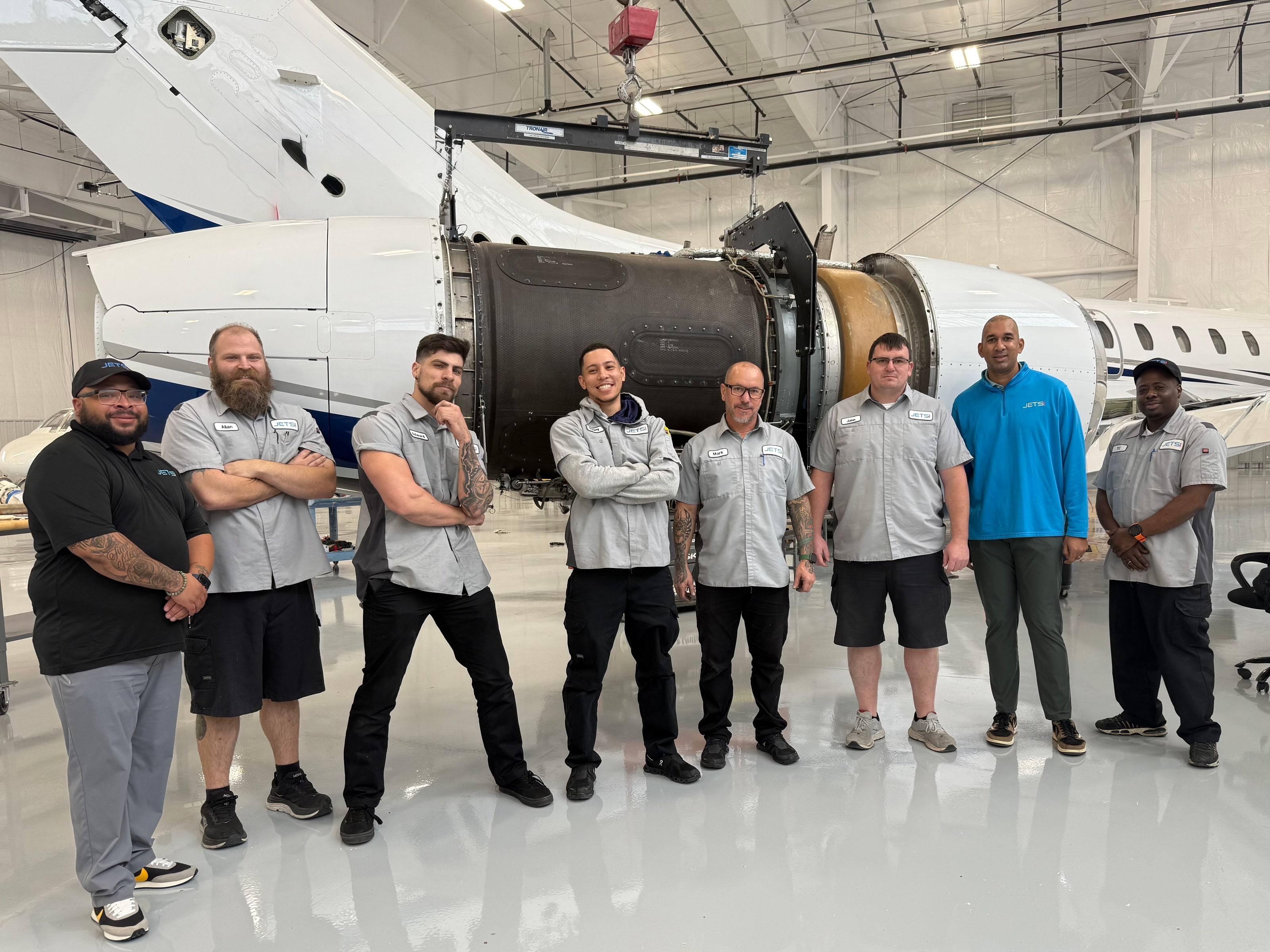Eight Jets MRO team members in front of a jet engine held on a hoist during an engine change in the hangar