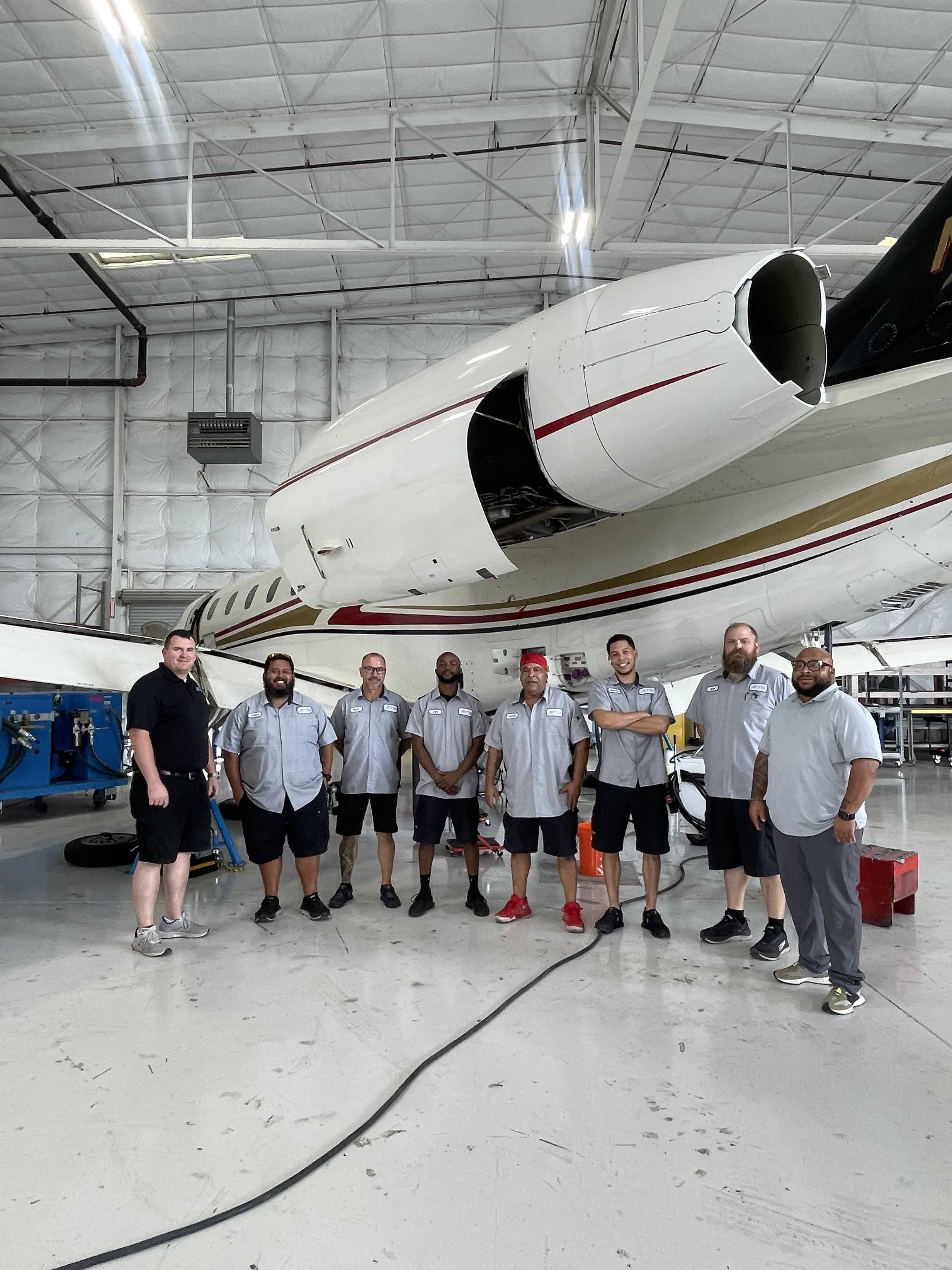 Eight Jets MRO technicians and staff lined up in the hangar beneath a business jet with an engine cowling open